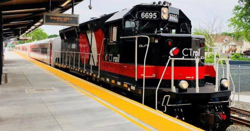 A CTrail locomotive at a train station, with a passenger train on the adjacent track and a platform in the foreground.