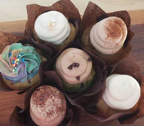 A variety of six decorated cupcakes with colorful frosting and toppings, arranged in brown paper wrappers.