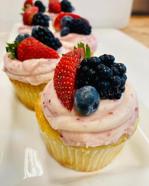 Close-up of cupcakes topped with pink frosting and fresh strawberries, blackberries, and blueberries.
