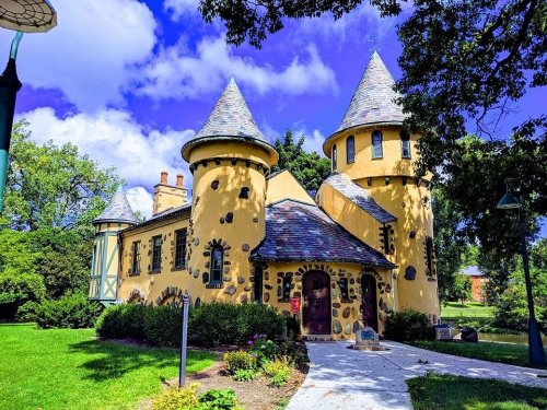 A whimsical yellow castle with stone accents and turrets, surrounded by green grass and trees under a blue sky.