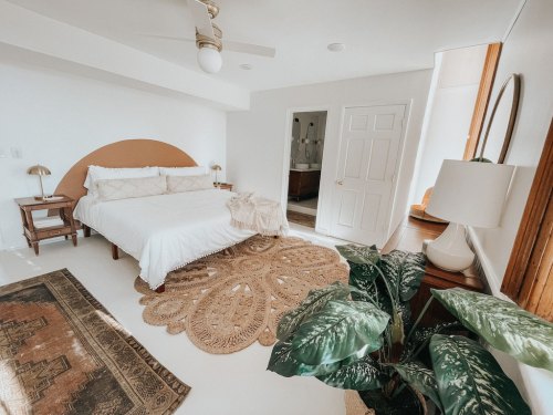 Bright, modern bedroom featuring a bed, decorative rug, plants, and natural light from a window.