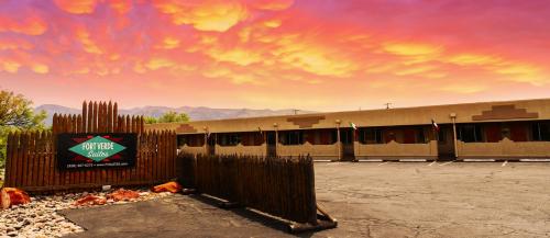 A colorful sunset over a motel with a wooden fence and a sign reading "Fox New Suites." Mountains in the background.
