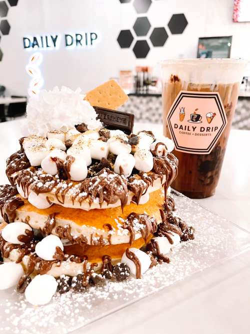 A decadent dessert stack with chocolate, marshmallows, and graham crackers, alongside a cold drink from Daily Drip.