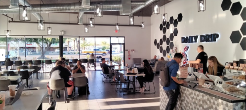 A modern café interior with hexagonal decor, patrons seated, and a counter displaying pastries and coffee.