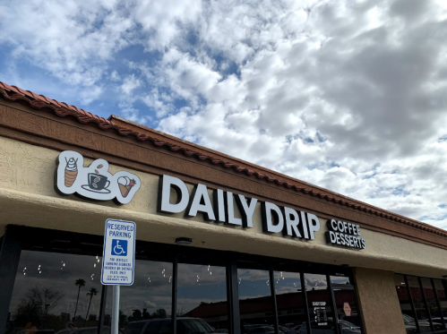 Sign for "Daily Drip" coffee and desserts shop, featuring a cartoon coffee cup and dessert icons, under a cloudy sky.
