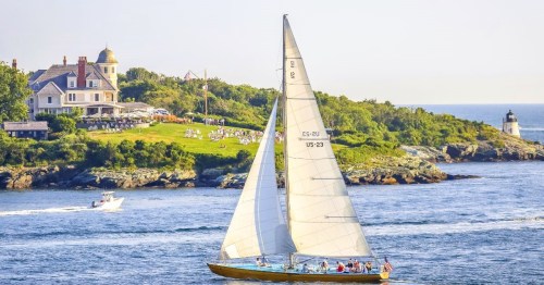 A sailboat on Narragansett Bay in Newport RI, with a scenic coastal landscape, featuring a large house and a lighthouse.