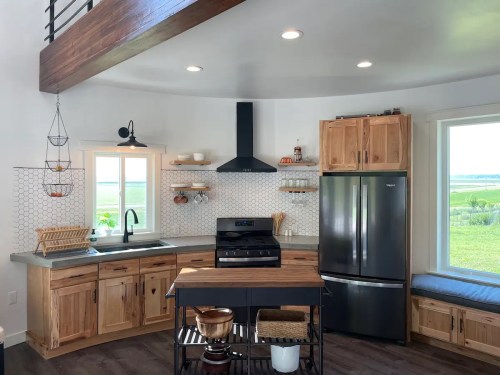 Modern kitchen with wooden cabinets, stainless steel appliances, and a cozy seating area by the window. Bright and airy design.