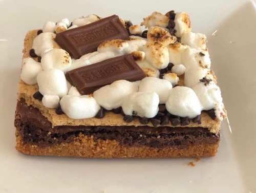 A delicious dessert bar with layers of chocolate, graham cracker, and topped with marshmallows and chocolate pieces.