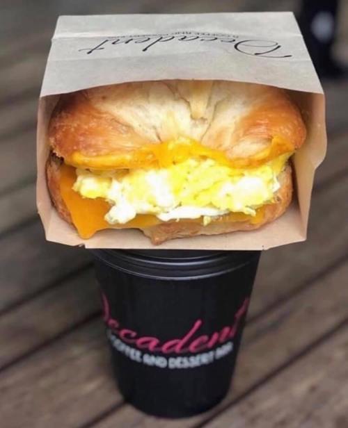 A croissant sandwich filled with scrambled eggs and cheese, placed on top of a coffee cup.