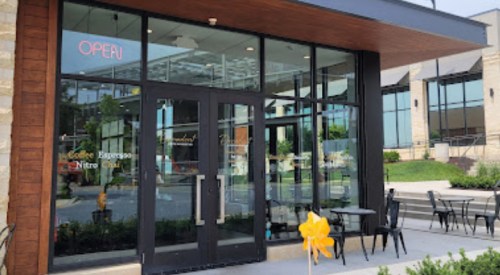 Exterior view of a coffee shop with large glass doors, a "OPEN" sign, and outdoor seating.