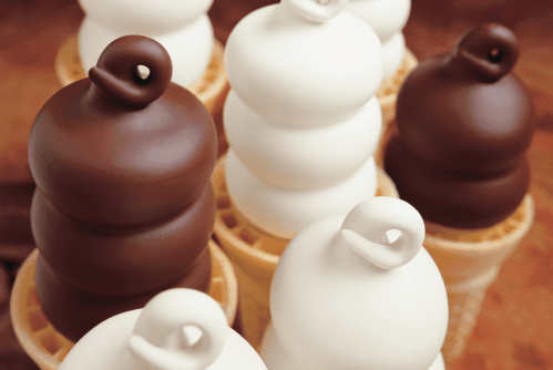 Close-up of ice cream cones with swirls of chocolate and vanilla soft serve stacked on top of each other.