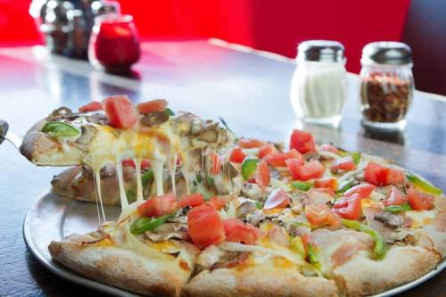 A freshly baked pizza topped with tomatoes, green peppers, and melted cheese, with a slice being lifted.