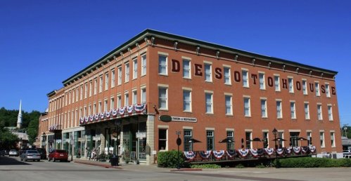 Historic DeSoto House Hotel with patriotic decorations, surrounded by greenery and a clear blue sky.