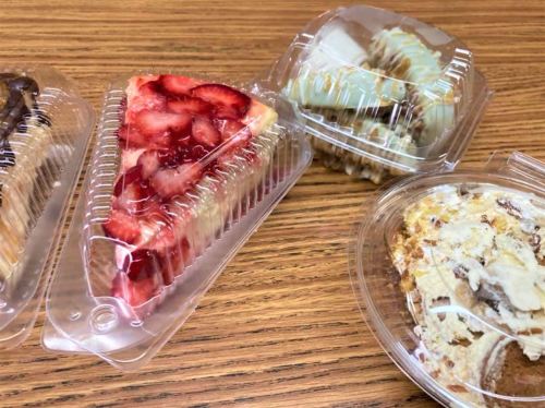Four desserts in clear containers: a strawberry cheesecake slice, a mint dessert, and two other assorted treats.