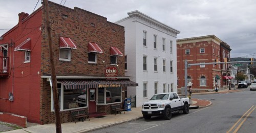 A street view featuring a brick building with awnings, a white building, and a parked truck on a cloudy day.