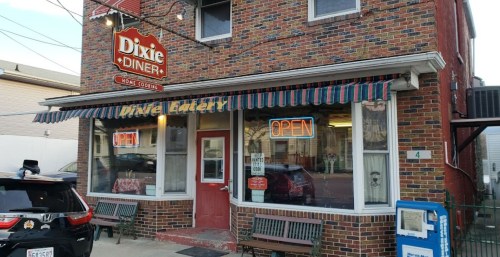 A brick diner with a striped awning, "Dixie Diner" sign, and an "OPEN" neon sign, featuring outdoor seating.
