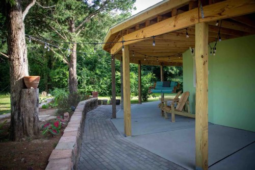 A cozy outdoor patio with wooden furniture, string lights, and a lush green backdrop.