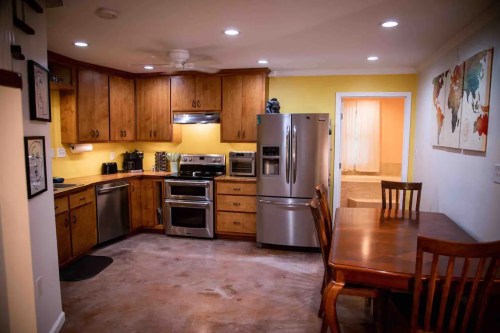 A modern kitchen with wooden cabinets, stainless steel appliances, and a dining table, featuring warm yellow walls.