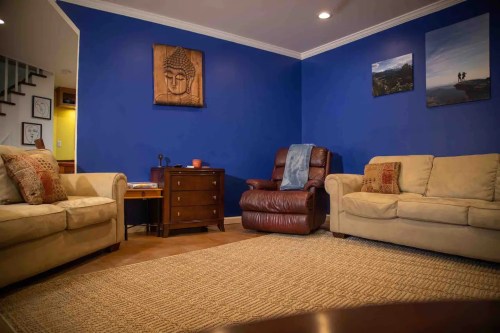 Cozy living room with blue walls, two beige sofas, a brown recliner, a wooden table, and decorative wall art.