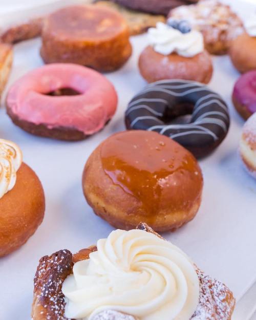 A variety of colorful donuts with different toppings and fillings arranged on a white surface.
