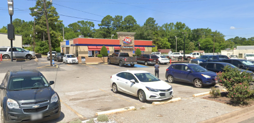 A Dairy Queen restaurant with a parking lot filled with various cars and trees in the background on a sunny day.