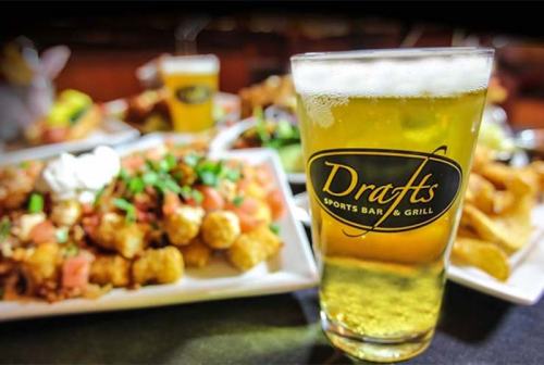 A glass of beer in front of a plate of nachos and tater tots at Drafts Sports Bar & Grill.