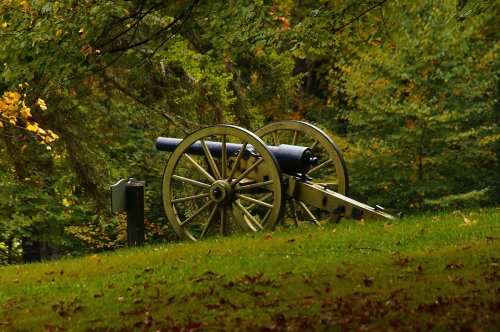 A historic cannon on a grassy hill, surrounded by trees with autumn foliage.