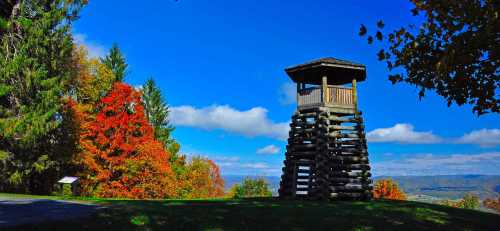 A wooden observation tower surrounded by vibrant autumn foliage under a blue sky with scattered clouds.