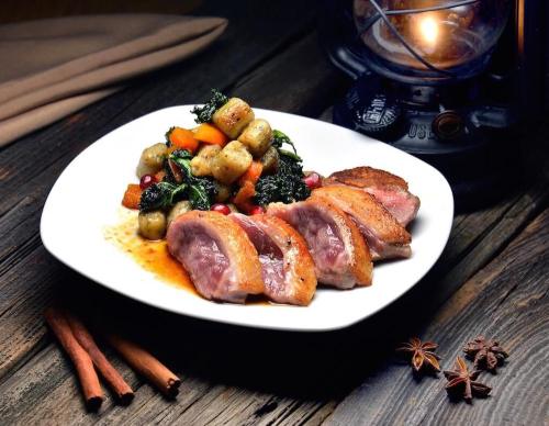 A plate of sliced duck breast with a colorful vegetable and gnocchi medley, set beside a lantern and spices.