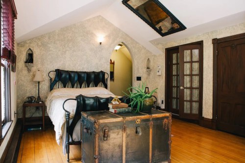 Cozy bedroom with a bed, vintage trunk, and decorative plants, featuring sloped ceilings and warm wooden floors.