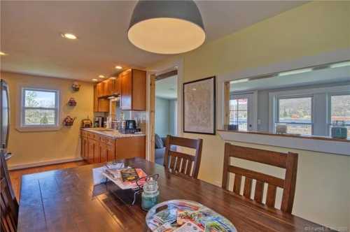 A cozy kitchen and dining area with wooden furniture, a light fixture, and a view of the outdoors through large windows.