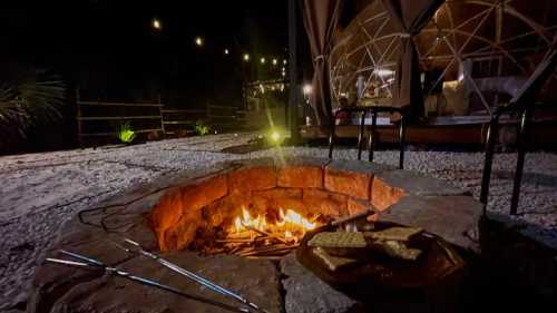 A cozy campfire surrounded by stones, with s'mores ingredients nearby, set in a dimly lit outdoor space.