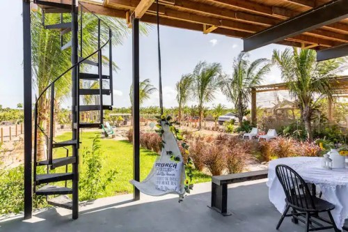 A cozy outdoor space with a spiral staircase, swing, and lush greenery in the background under a sunny sky.