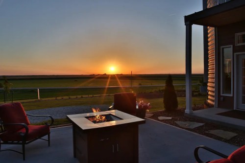 A sunset view over a grassy landscape, with a fire pit and red chairs in the foreground.