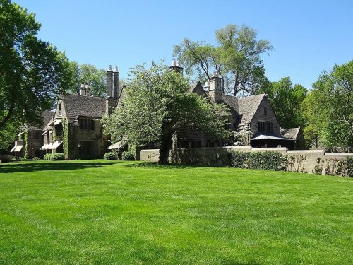 A large, elegant stone mansion surrounded by lush green grass and trees under a clear blue sky.