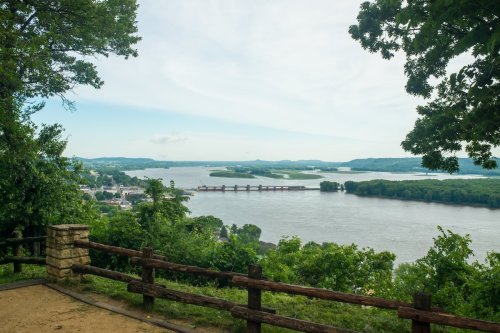 Scenic view of a river with lush greenery and a distant bridge, under a cloudy sky.