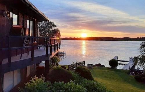 A serene sunset over a lake, viewed from a balcony with lush greenery and a dock in the distance.