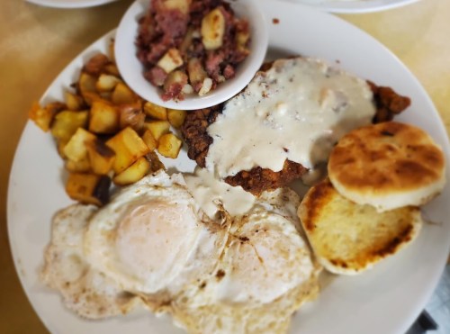 A plate of breakfast featuring fried chicken with gravy, two eggs, hash browns, and a biscuit.