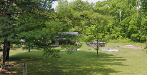 A grassy area with a small building, a pool, and trees in a lush green landscape.