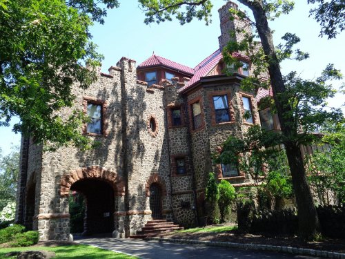 A large stone castle with a red roof, surrounded by trees and greenery, showcasing intricate architectural details.