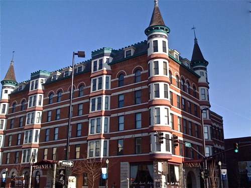 Historic brick building with turrets and green accents, set against a clear blue sky.
