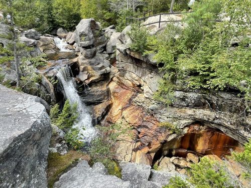 A serene waterfall cascades over rocky terrain, surrounded by lush greenery and rugged stone formations.