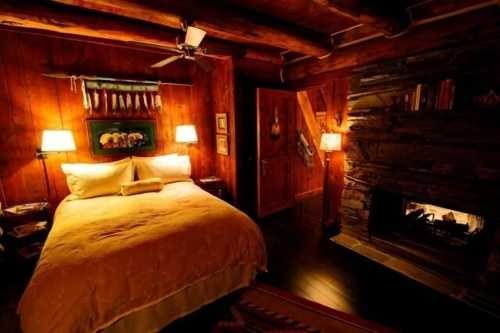 Cozy bedroom with a wooden interior, a large bed, lamps, and a fireplace, creating a warm, inviting atmosphere.