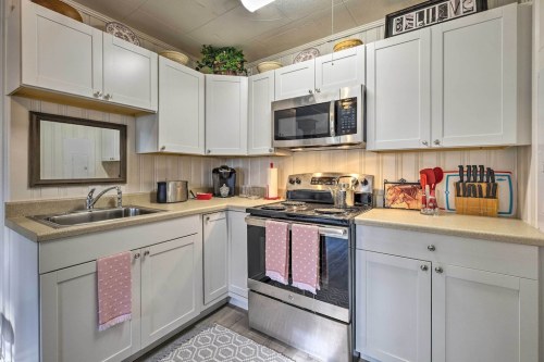 A modern kitchen with white cabinets, stainless steel appliances, and pink accents, featuring a sink and stove.