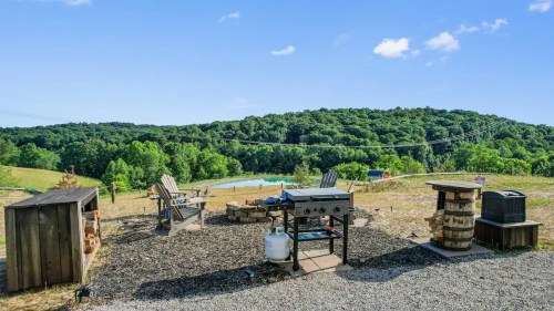 A scenic outdoor area with a grill, seating, and a view of green hills and a pond in the background.