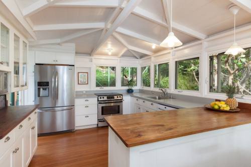 Bright kitchen with white cabinets, stainless steel appliances, and a wooden island, surrounded by large windows.