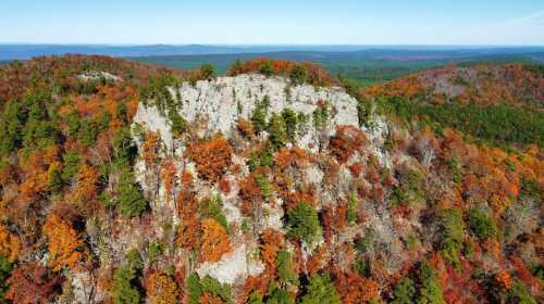 Aerial view of a rocky outcrop surrounded by vibrant autumn foliage in a mountainous landscape.