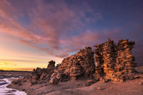 Rock formations at sunset, with layered stones illuminated by warm light against a colorful sky.
