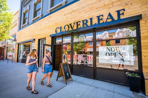 Two women walk past a storefront with a wooden facade and a sign that reads "CLOVERLEAF" and "NOW OPEN."