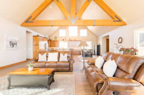 Spacious living room with leather sofas, wooden beams, and a view of an open kitchen in a bright, airy setting.